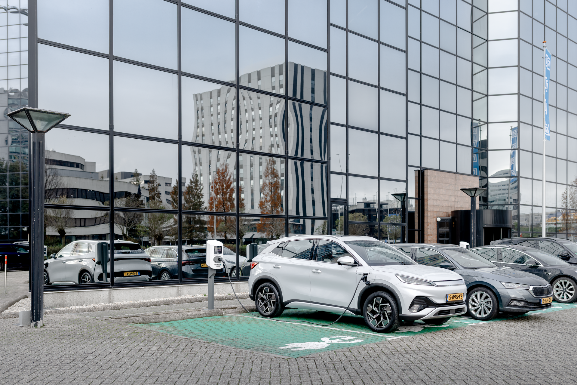 Auto's geparkeerd op een parkeerplaats voor een gebouw met een laadpaal
